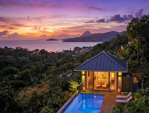 A villa with a pool, surrounded by lush greenery and overlooking a body of water with distant mountains.