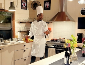 A chef in a white uniform standing in a kitchen with a stove, pots, and a coffee machine.