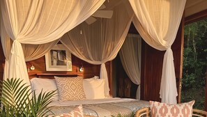A bedroom with a canopy bed, a bedside table, a mirror, and a view of greenery outside.