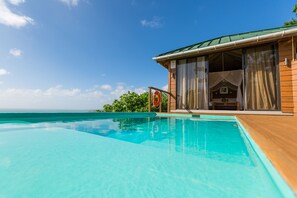 Blick auf einen Poolbereich eines Resorts mit Holzterrasse, Rettungsboje und Meerblick.