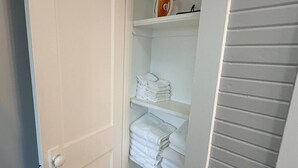 Een kast met planken, gevuld met opgevouwen handdoeken en een hangijzer.