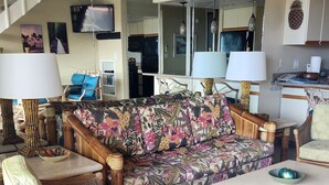Een ruime zithoek met een bank, twee fauteuils, een salontafel en een keuken op de achtergrond.