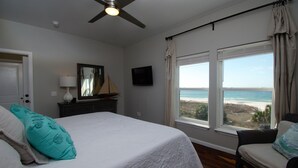 Un dormitorio con cama, ventilador de techo, cómoda, televisor y vista al océano.