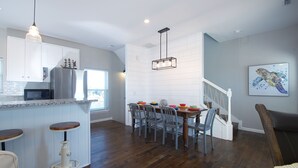 Una cocina moderna con una isla central, taburetes de bar y un comedor con sillas.