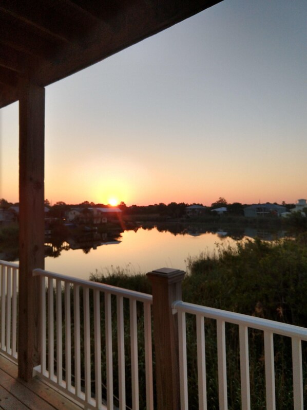 A sunset over a calm body of water with a wooden deck and railing in the foreground.