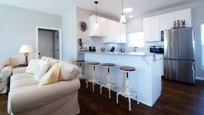 Una cocina moderna con armarios blancos, un refrigerador de acero inoxidable y una zona de bar con taburetes.