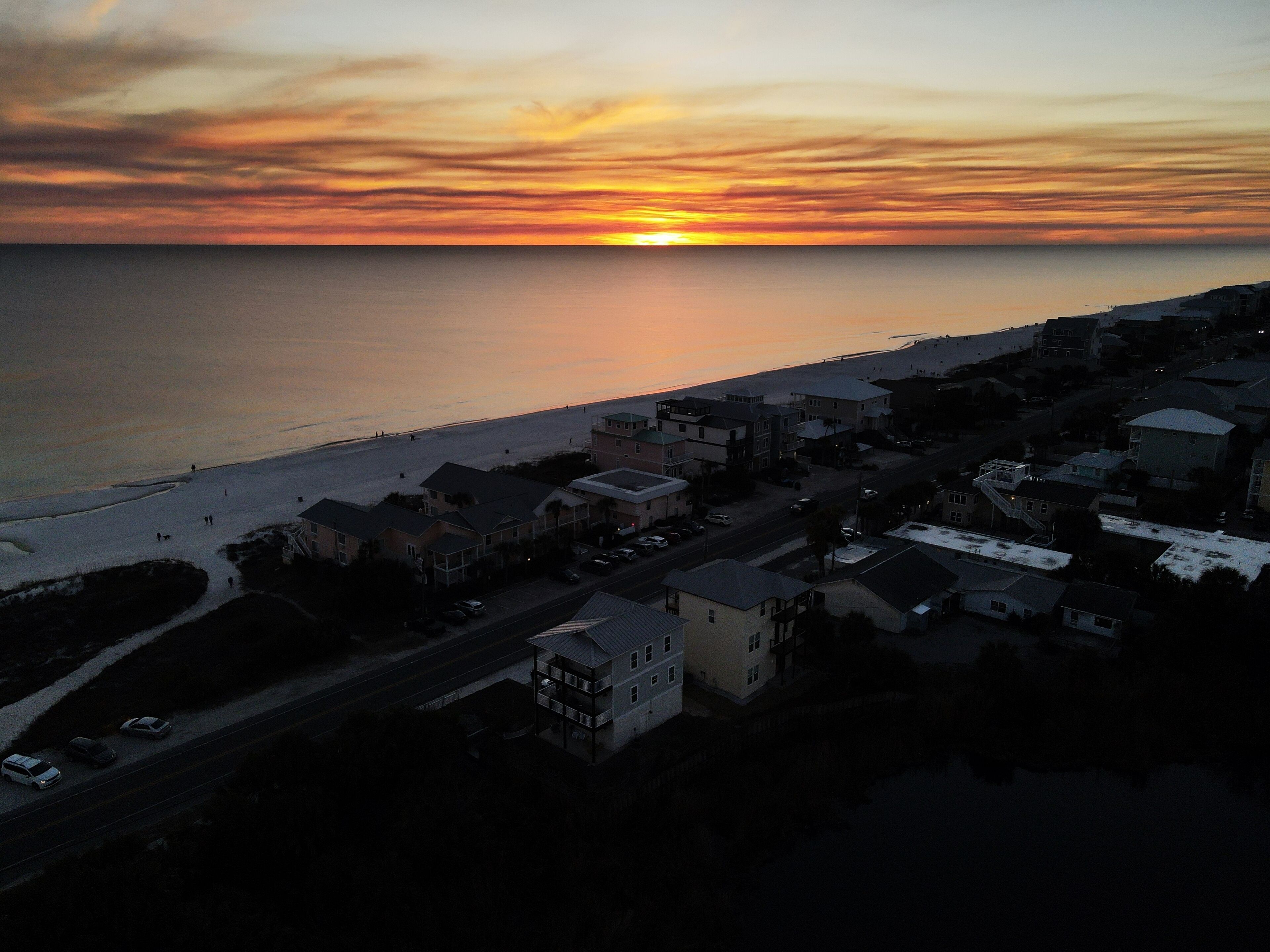 An aerial view of a coastal town with a beach, houses, and a road.