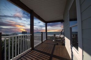 A covered balcony with a view of the sunset over the ocean.