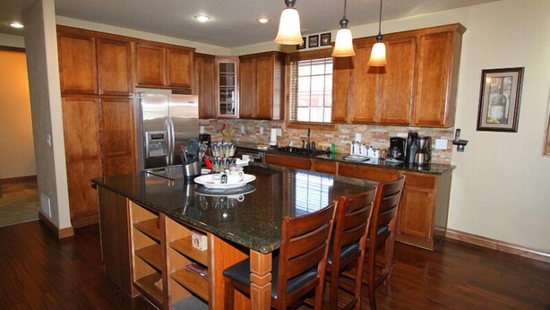 A kitchen with wooden cabinets, a central island with chairs, and a refrigerator.