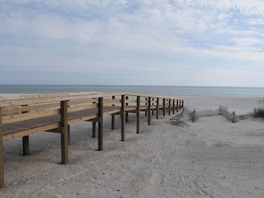 A wooden boardwalk leading to a sandy beach with the ocean in the background.