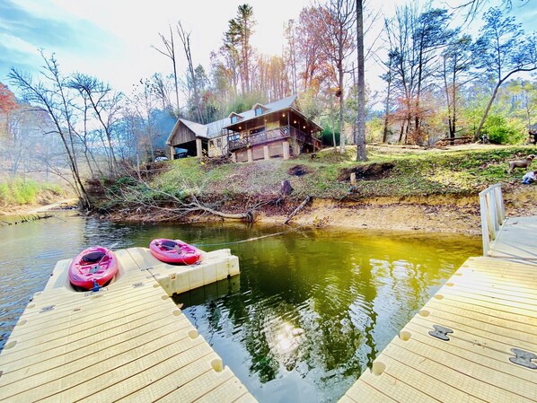 Un muelle de madera con kayaks y una casa al fondo.