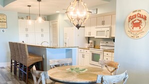 A kitchen with white cabinets, a dining area with a round wooden table and chairs, and a hanging light fixture. - Tradewind Mexico Beach 2/2 with balcony beach view (Mexico Beach)