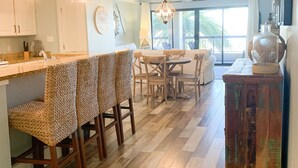 A modern kitchen with a bar area, wooden flooring, and a dining space with a view. - Tradewind Mexico Beach 2/2 with balcony beach view (Mexico Beach)