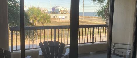 Ein Zimmer mit einer großen Glasschiebetür, die auf einen Balkon mit Sitzgelegenheit und Blick auf Strand und Gebäude führt.