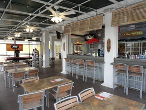 A restaurant interior with high ceilings, metal chairs, wooden tables, and a bar area.