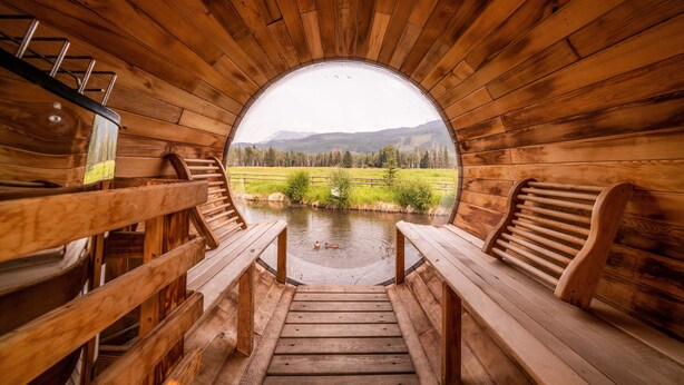 Interior de madera con un ventanal circular que ofrece vistas de un río y montañas.