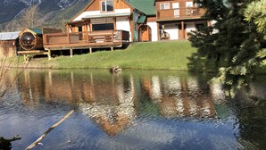 Una cabaña de madera con un balcón que da a un lago, rodeada de montañas.