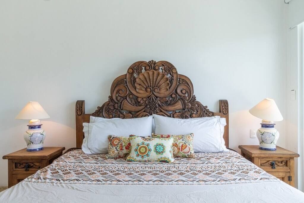 A bed with a patterned bedspread, two bedside tables with lamps, and a decorative headboard.