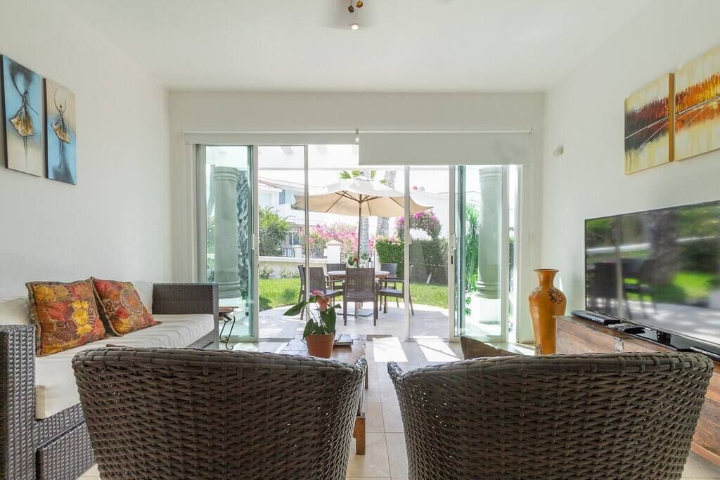 A spacious living room with a large TV, wicker furniture, and a glass door leading to an outdoor patio.