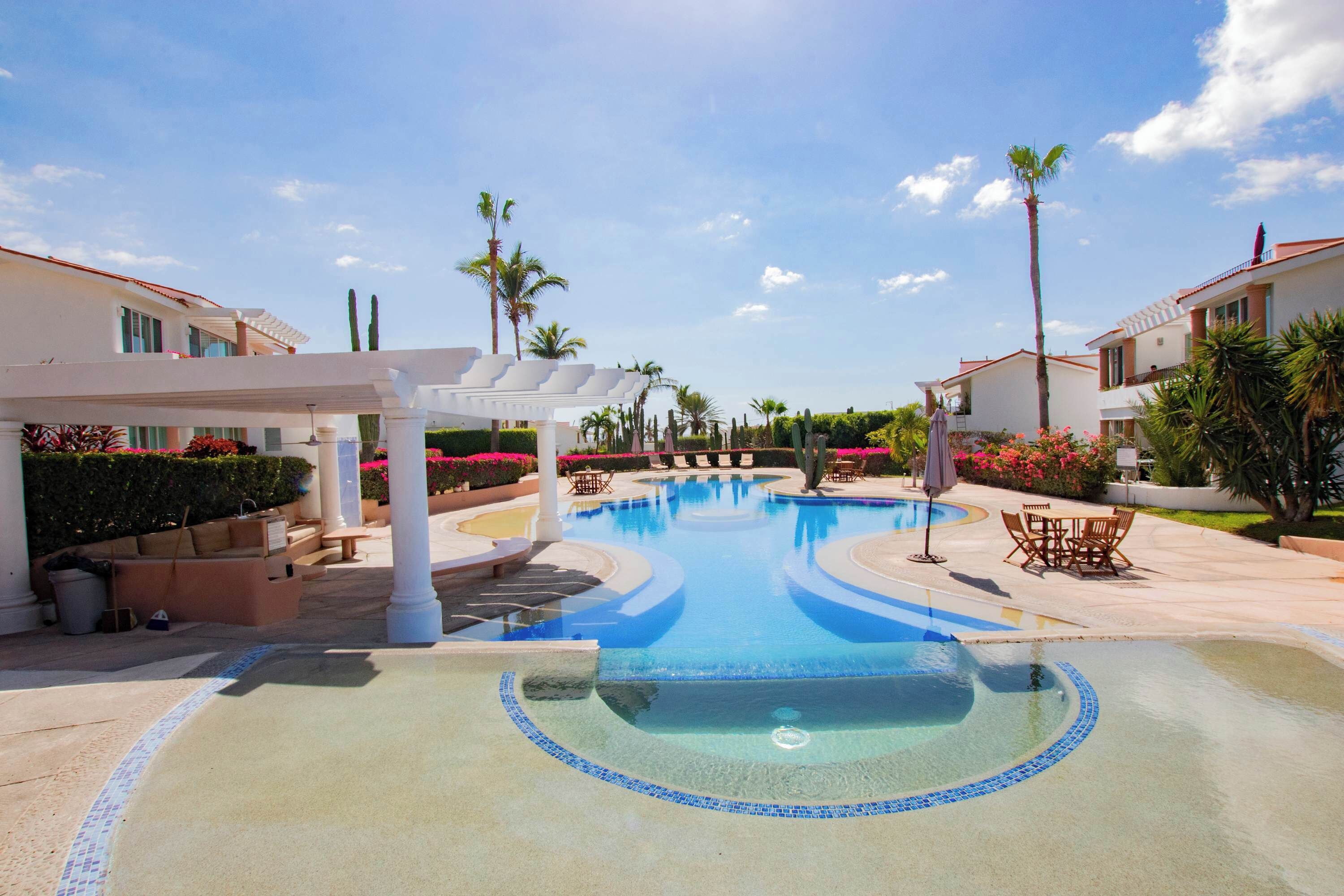 A swimming pool with a tiled edge, surrounded by lounge chairs and palm trees.