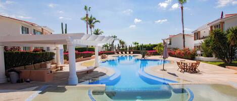 A swimming pool with a tiled edge, surrounded by lounge chairs and palm trees.