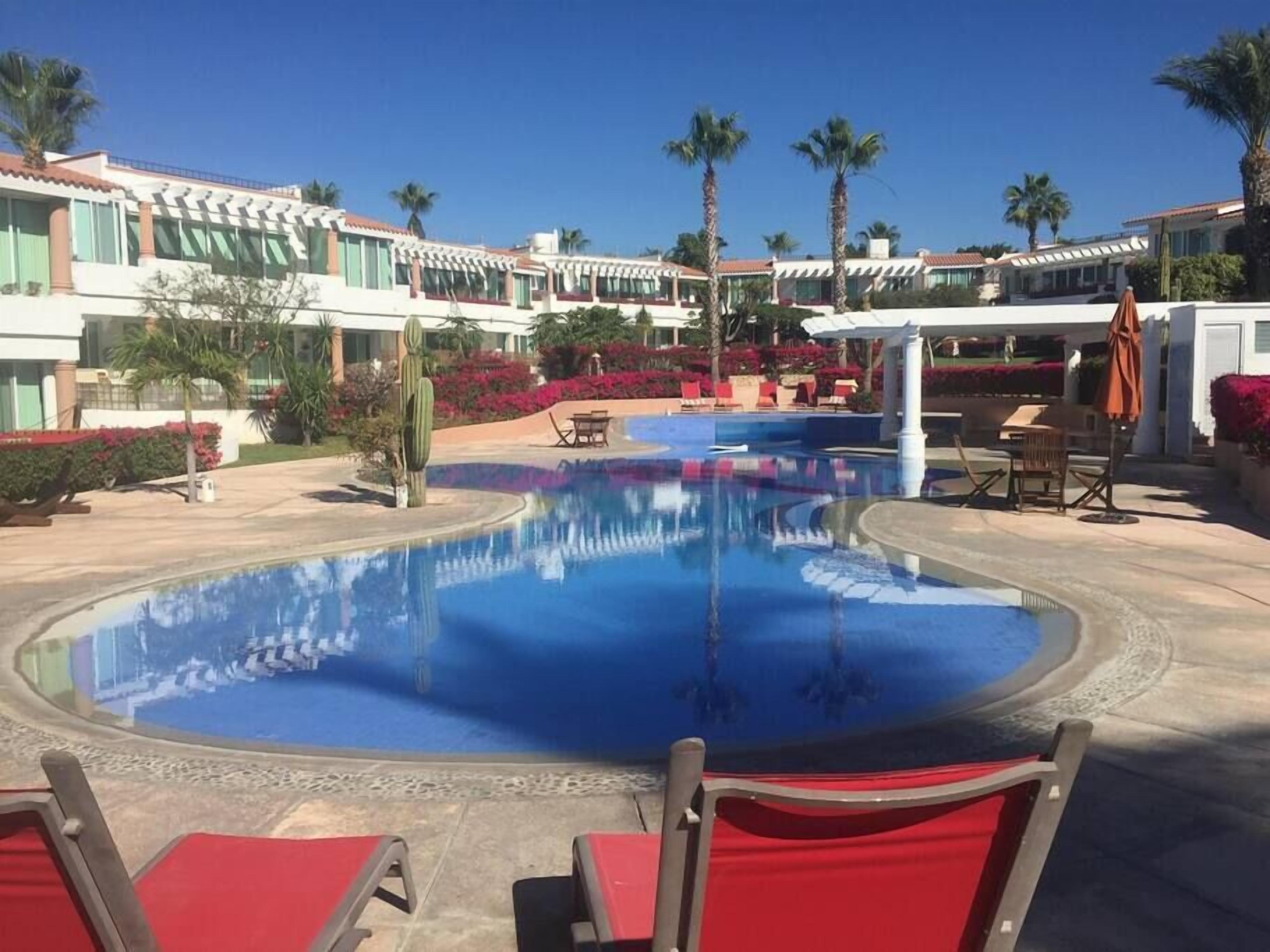 A pool area with lounge chairs, palm trees, and a building with a tiled roof.