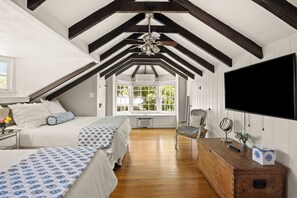 A bedroom with a sloped ceiling, a bed, a chair, a TV, and a window with a view of greenery. - Historic Luxury Estate for 13 - Heated Pool, Hot Tub, Fire Pit & Pool Table (Fredericksburg)