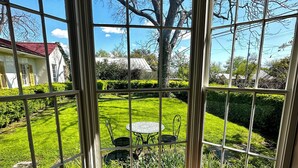 Une pièce dotée d’une grande fenêtre donnant sur un jardin bien entretenu, avec une pelouse, une table et des chaises.