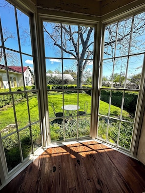 A room with a large window offering a view of a well-maintained garden with a lawn, a table, and chairs.