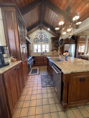 A kitchen with wooden cabinets, a granite countertop, a stainless steel refrigerator, and a hanging pot rack. - Historic Luxury Estate - Heated Pool, Hot Tub, Fire Pit & Pool Table for 13 (Fredericksburg)