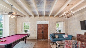 A wooden pool table with balls, a blue sofa with a cushion, a chandelier, and a stone wall. - Historic Luxury Estate - Heated Pool, Hot Tub, Fire Pit & Pool Table for 13 (Fredericksburg)