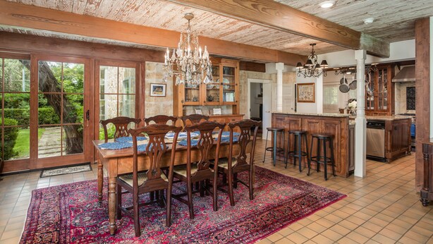 A spacious dining area with a wooden table and chairs, a chandelier, and a large window overlooking a garden. - Historic Luxury Estate - Heated Pool, Hot Tub, Fire Pit & Pool Table for 13 (Fredericksburg)