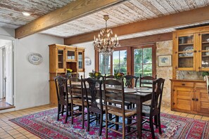 A dining room with a wooden table, chairs, and a chandelier. There are cabinets with glass doors and a rug on the floor. - Historic Luxury Estate for 13 - Heated Pool, Hot Tub, Fire Pit & Pool Table (Fredericksburg)