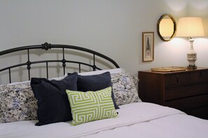 A neatly made bed with a patterned pillow, a bedside lamp, and a dresser with a mirror.