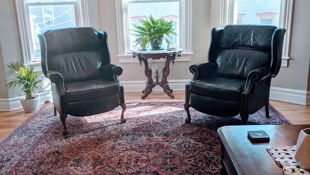 A living room with two black leather chairs, a wooden coffee table, a patterned rug, and a small table with a plant.
