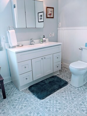 A bathroom with a white vanity, a sink, a mirror, a toilet, and patterned floor tiles.