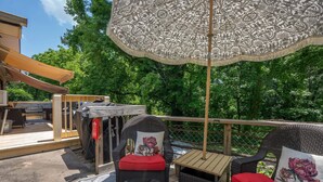 Eine Terrassenausstattung mit Korbstühlen, einem Tisch und einem gemusterten Sonnenschirm.