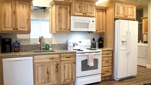 Una cocina con armarios de madera, un microondas blanco, una estufa, un refrigerador y un lavavajillas.