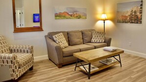 Una sala de estar con un sofá, una mesa de centro de madera, un sillón estampado y dos cuadros en la pared.