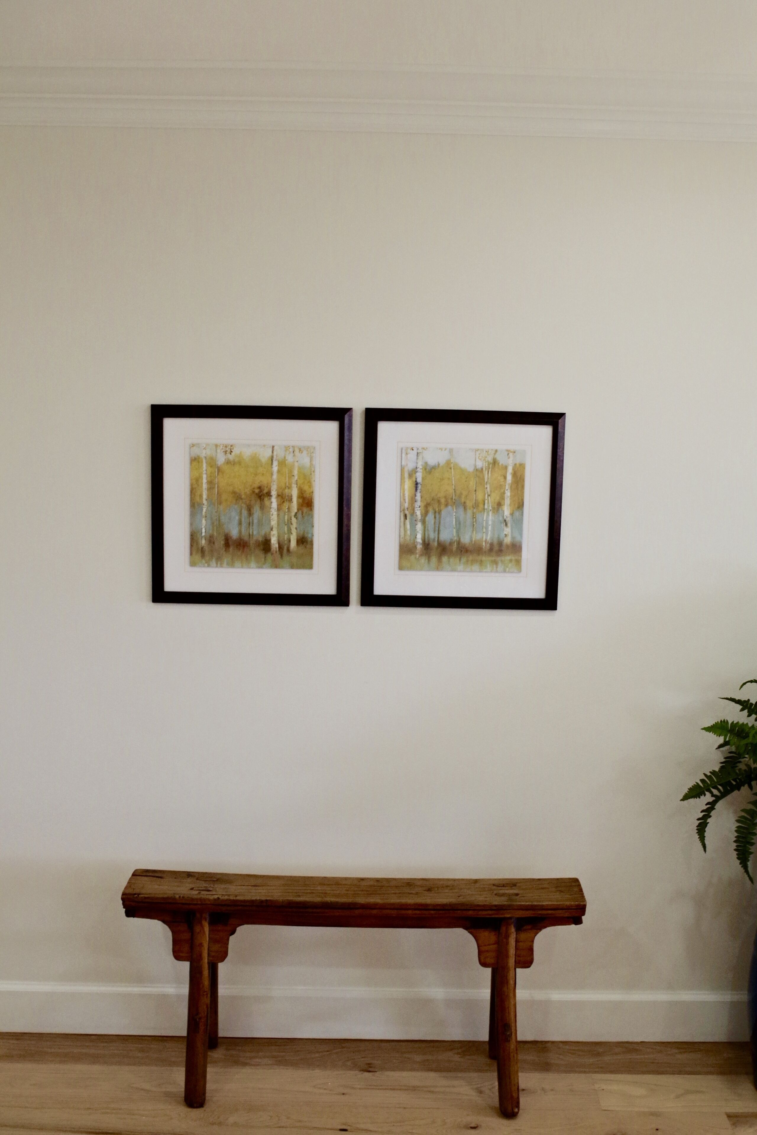 Een kamer met een houten bankje en twee ingelijste schilderijen aan de muur.