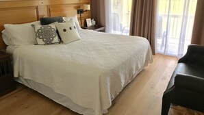 A hotel room with a large bed, a wooden headboard, a nightstand with a lamp, a chair, and a view of the outdoors through a window with curtains. - Tranquil tidal marsh setting (Seabrook Island)