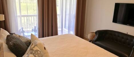 Habitación de hotel con cama, televisor, sofá y vista a una piscina por la ventana.