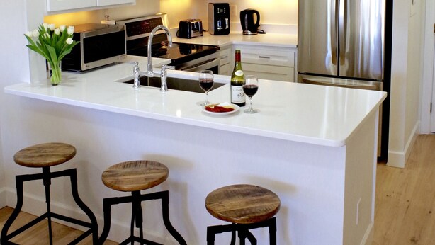 A modern kitchen with white cabinetry, a stainless steel refrigerator, a built-in oven, and a bar area with stools. - Tranquil tidal marsh setting (Seabrook Island)