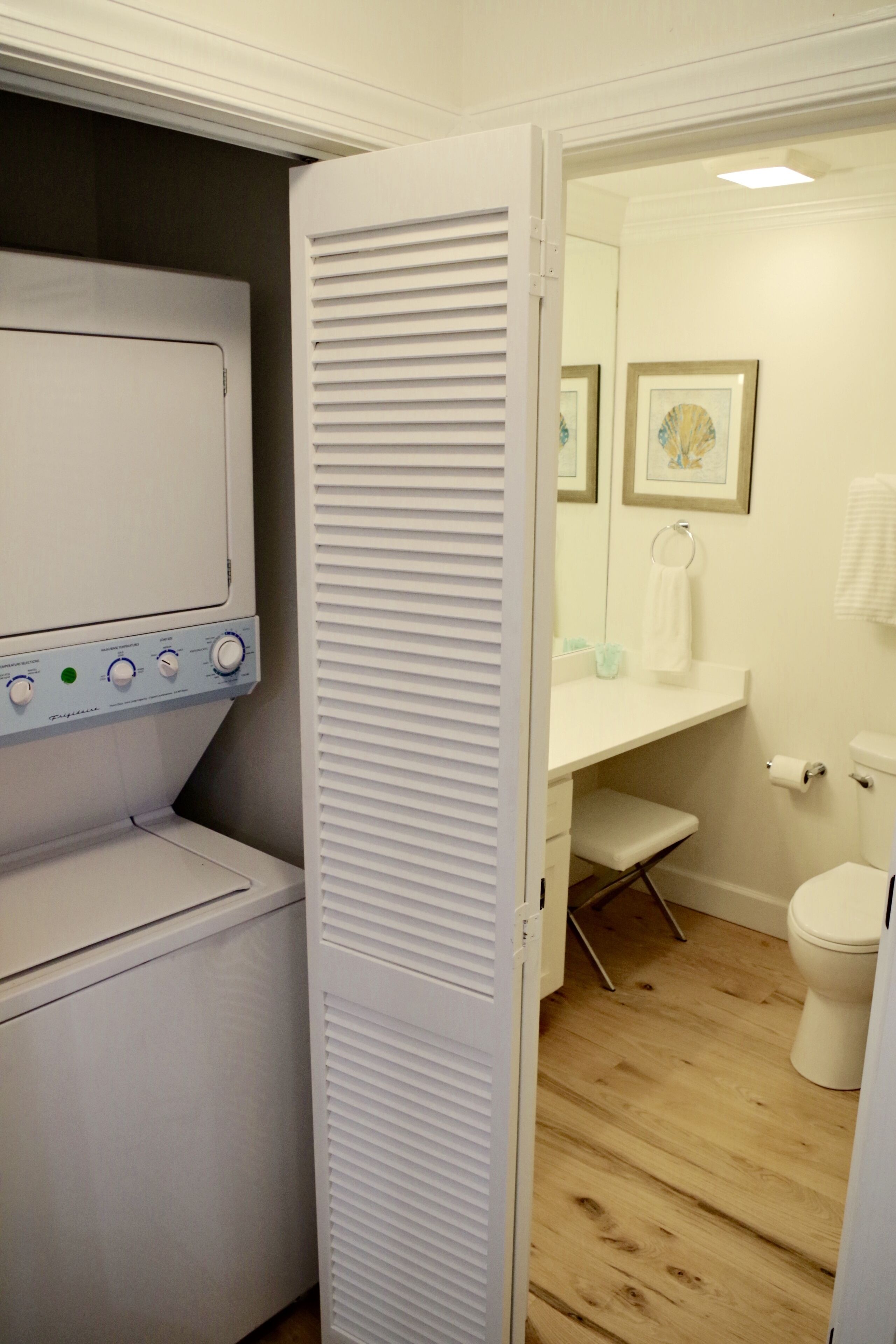 Une petite buanderie équipée d’un lave-linge et d’un sèche-linge à chargement frontal, d’un petit banc et de toilettes.