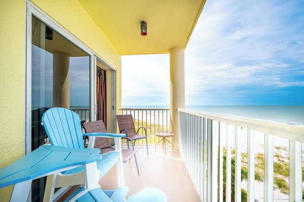 A balcony with blue chairs, a small table, and a view of the beach.
