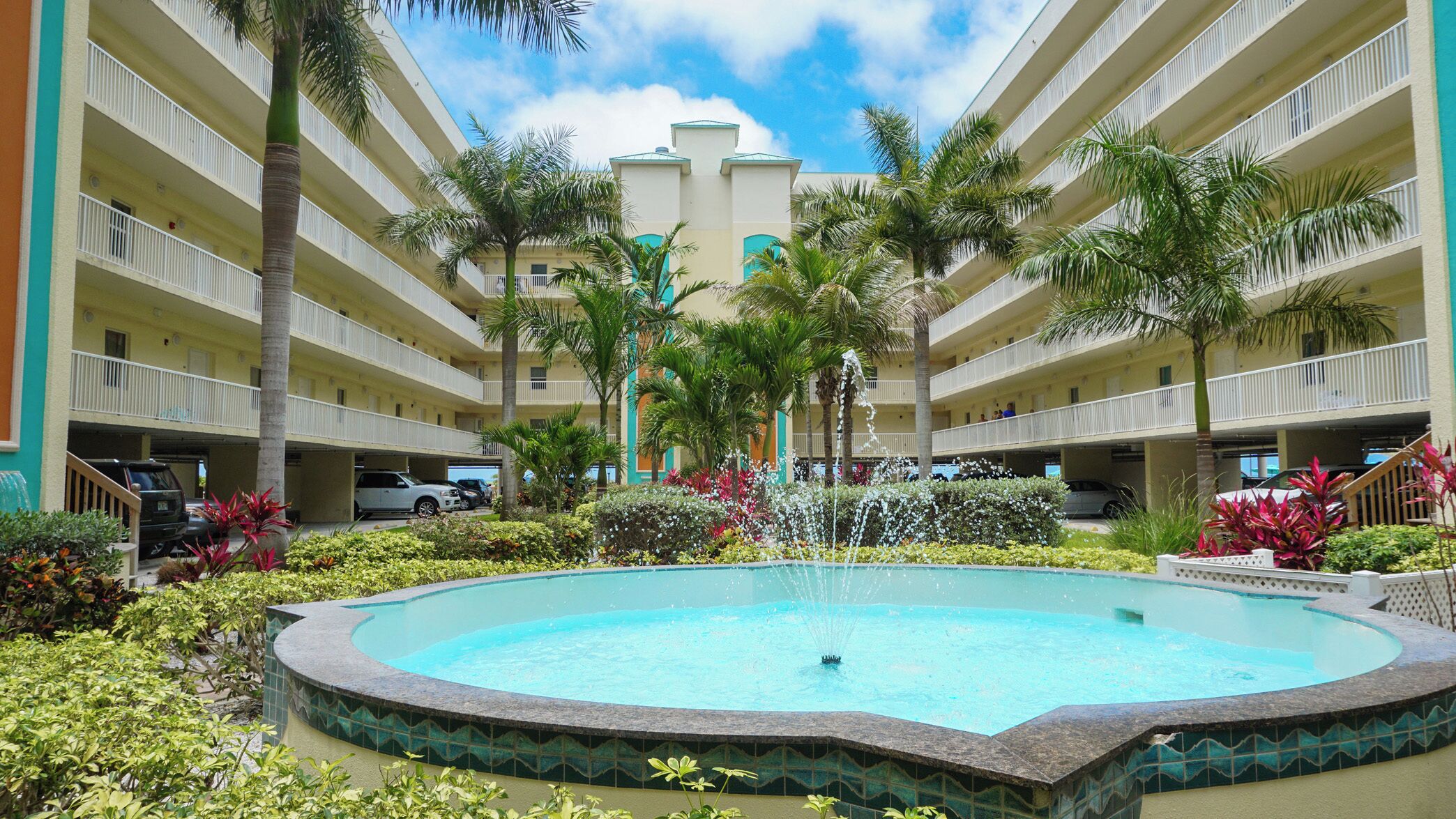 A hotel courtyard with a central fountain, multiple balconies, and a parking area.