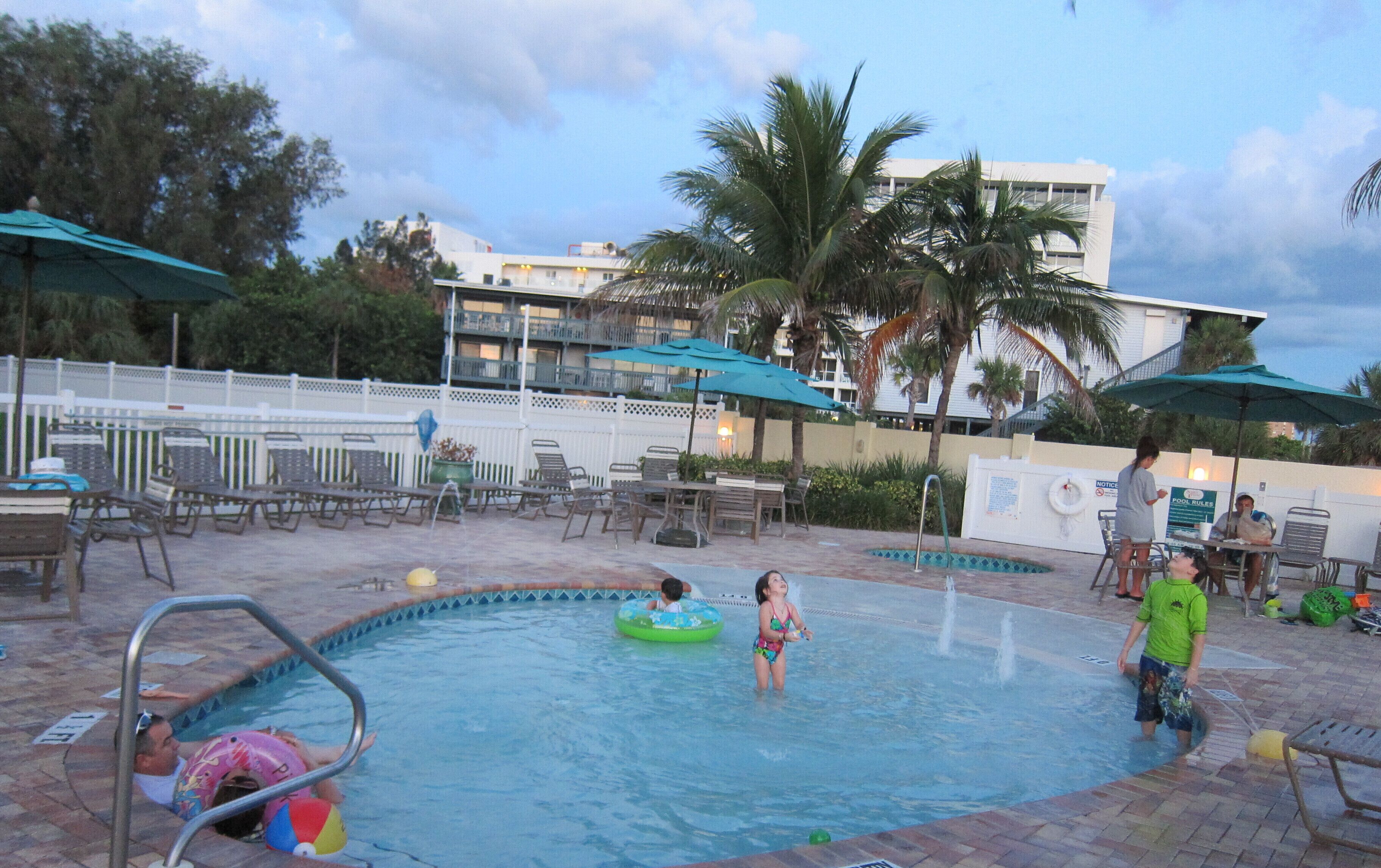 A swimming pool area with lounge chairs, umbrellas, and a poolside table.