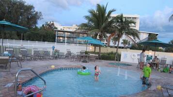 A swimming pool area with lounge chairs, umbrellas, and a poolside table.