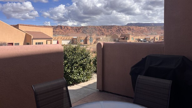 A patio with a table and chairs, a barbecue grill, and a view of a desert landscape with buildings in the background. - 1A8 Views, Shared Pool & Hot Tub, Private Patio & Garage (Moab)