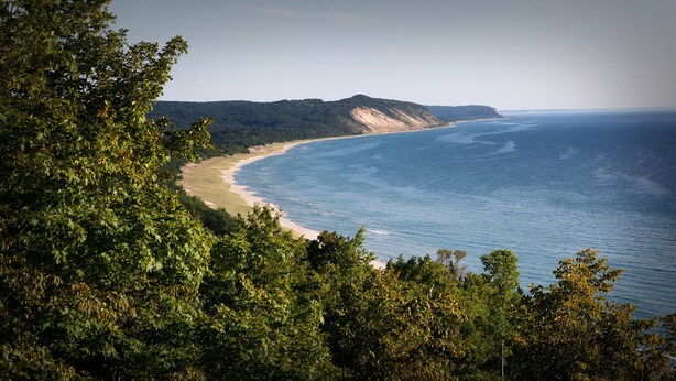 Un paisaje costero con una playa, colinas boscosas y una vista despejada del océano.